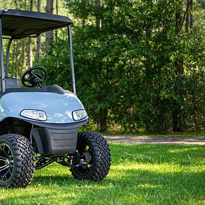 Golf cart with custom lift kit on grassy field in wooded area.